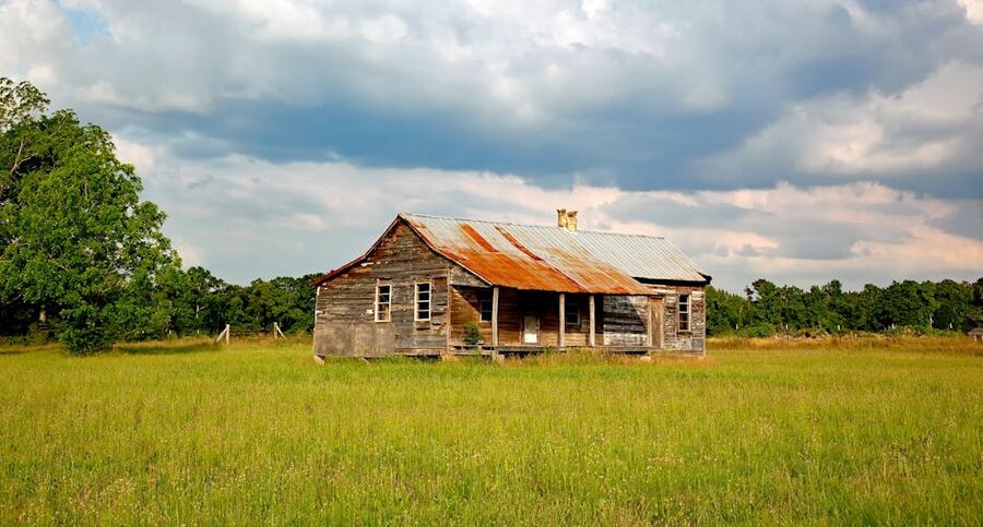 Old weathered farmhouse standing in a green field with trees