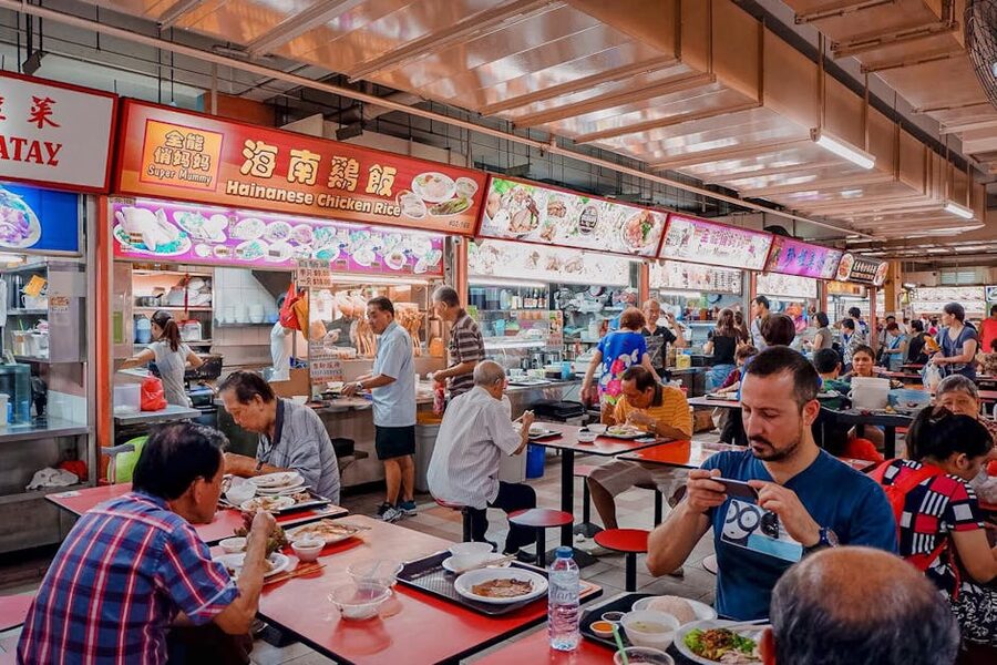 Diners eating at outdoor tables under the open-sided roof of Newton Food Centre hawker centre in Singapore