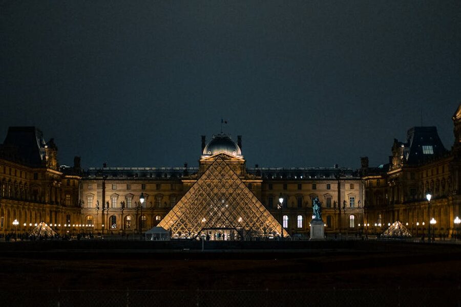 The Louvre Pyramid lit up at night with reflections in the surrounding pools