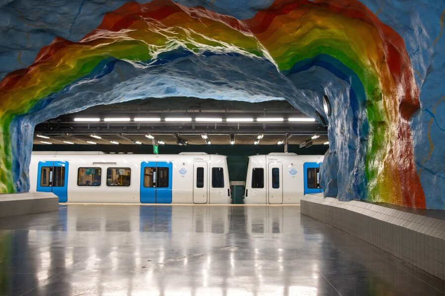 A colourful artwork-lined Stockholm metro station with passengers passing through