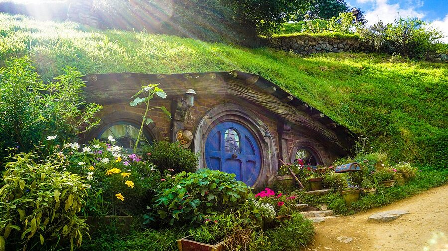Wide view of the Hobbiton movie set with hobbit holes set into the green hillside in Matamata