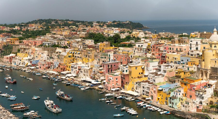 Aerial view of Procida island showing pastel-coloured houses tumbling toward Marina Corricella in the Bay of Naples